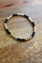 A beaded stretch bracelet with alternating black onyx and gold metallic beads, displayed on a warm brown wooden surface.