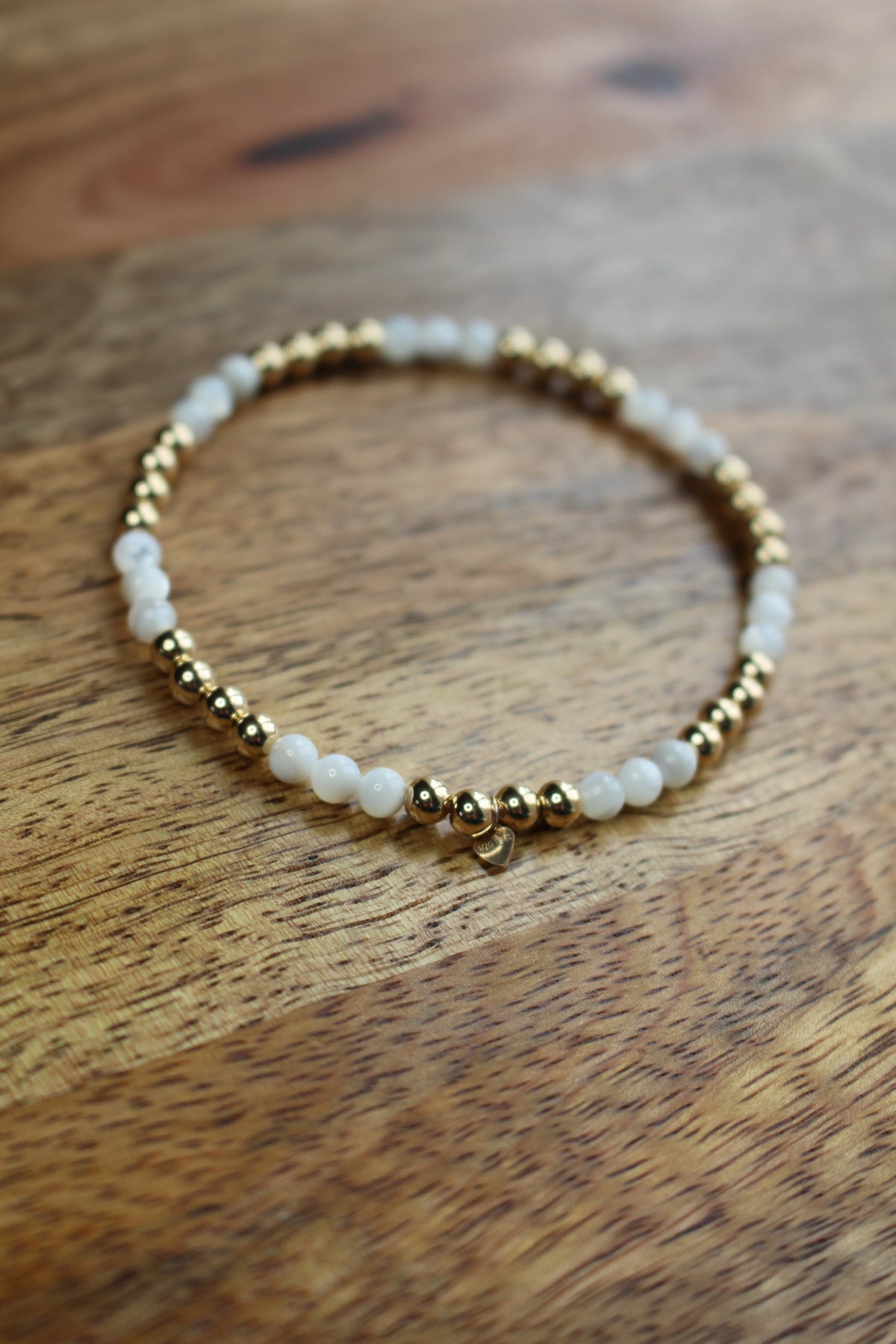A beaded stretch bracelet with white mother of pearl beads and gold spacer beads, resting on a wooden surface.